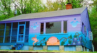 A small house painted purple and blue, with murals of fruit and vines along its foundation.