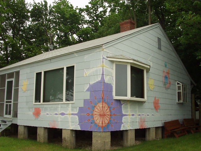 A pale grey house with a large violet and orange sunburst painted across its side wall.