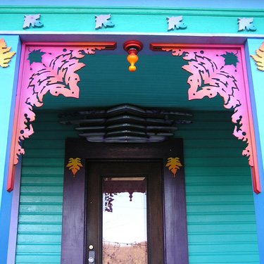A turquoise porch with carved brackets in fluorescent pink and orange framing the front door.