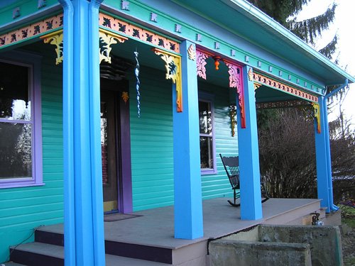 A turquoise house with bright blue porch columns and carved brackets along the eaves.