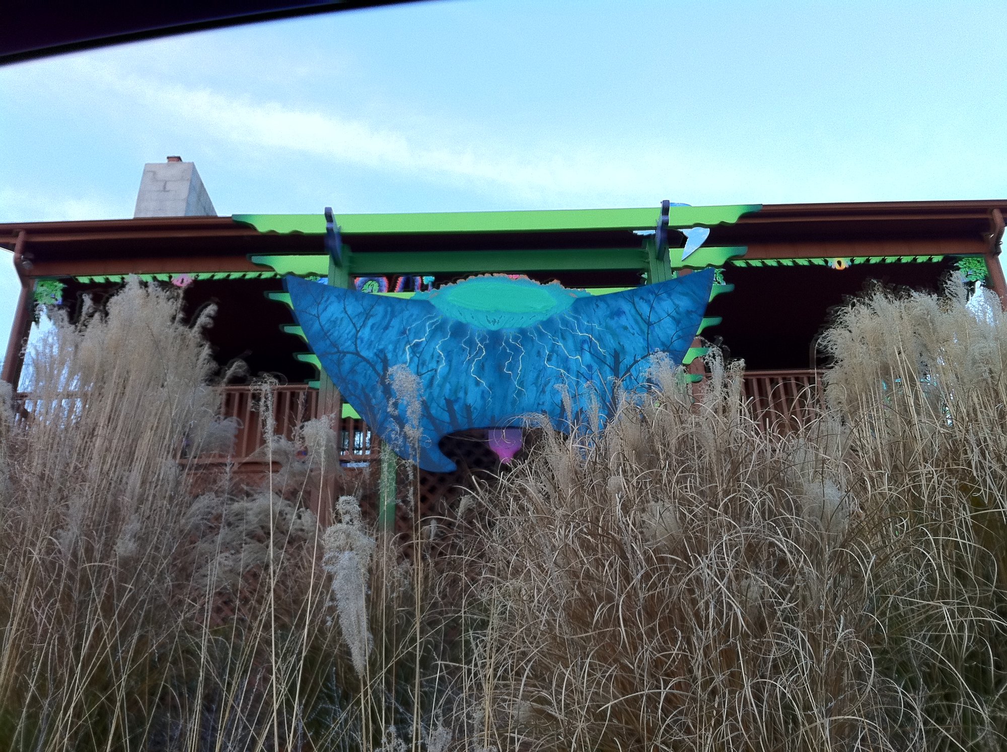 A blue sculpted form, like an open leaf, rising from tall grasses in front of the porch.