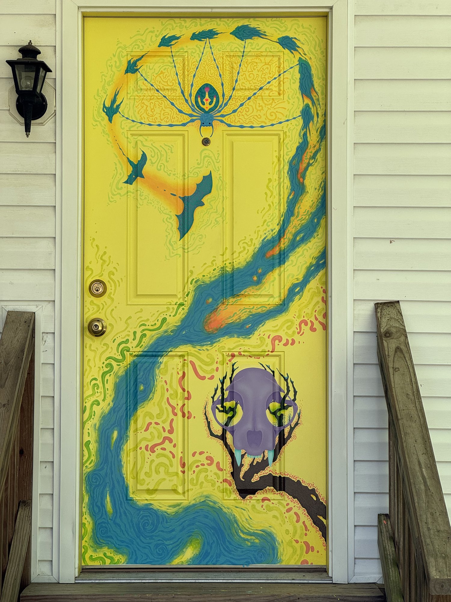A yellow side door painted with a flowing blue river, birds, and a spider in its web.