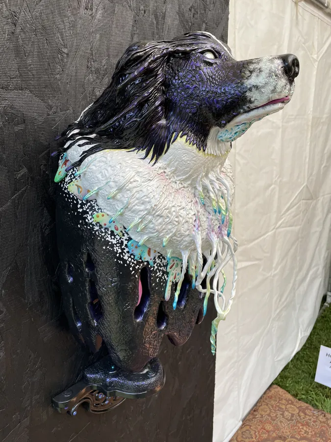A wall-mounted bust of a black-and-white dog with dripping white fur, on a black panel at the edge of the tent.