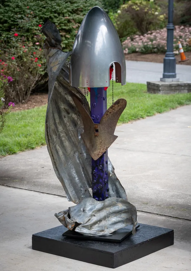 Avian Hourglass from the other side: the twisting metal sheet curls around the purple post, the rusted plow blade spreading like wings below the silver cone.