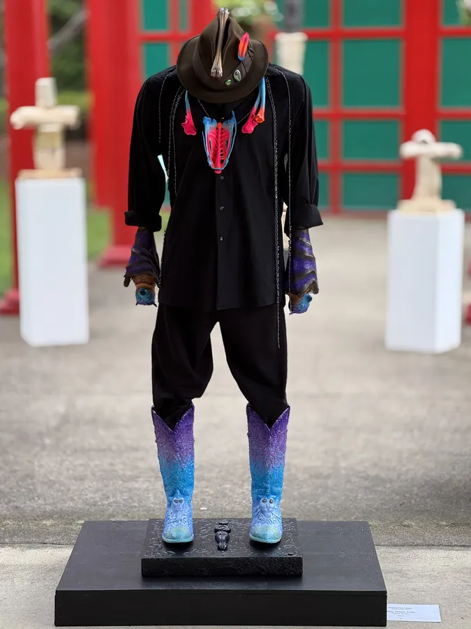 Big Nat's Hat from the front: a black suit with a patterned red shirt front, hat, painted hands, and purple-to-turquoise boots on a black base.