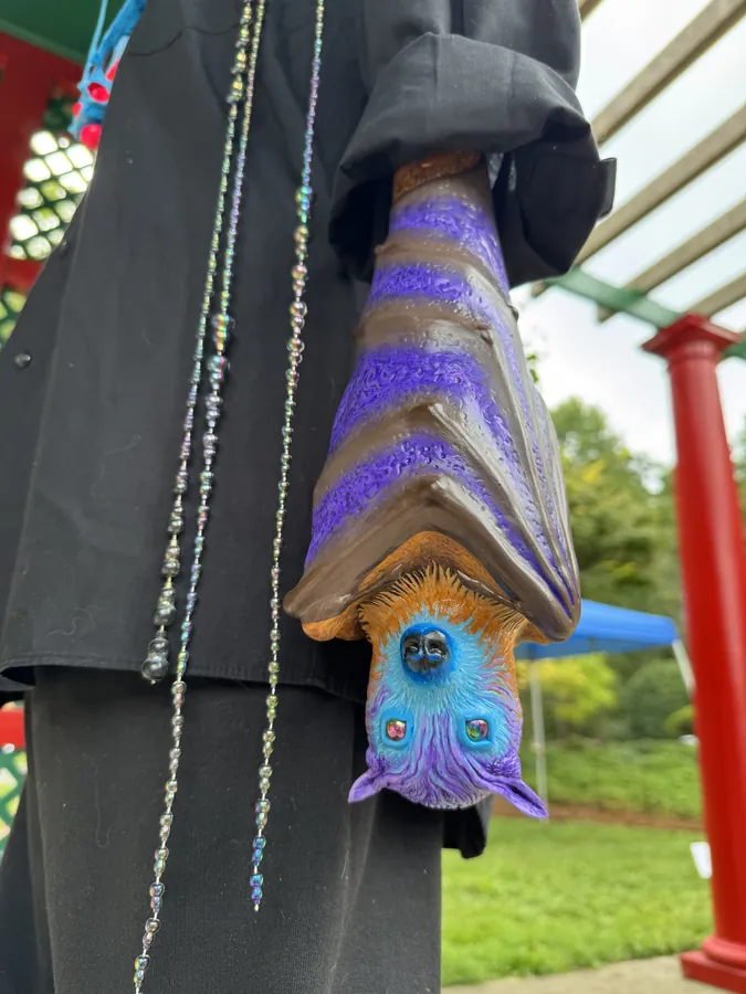 Detail of Big Nat's Hat: a painted bat hanging upside down against the black jacket, beaded strands beside it.