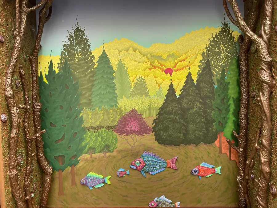 A closer view of the hutch's painted landscape, framed by carved bark-like vines, with fish swimming through the grass under a red sun.