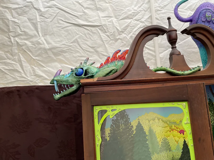 A green dragon with a blue eye and open jaws coils along the carved top of the hutch above the lime-green trim of its glass door.