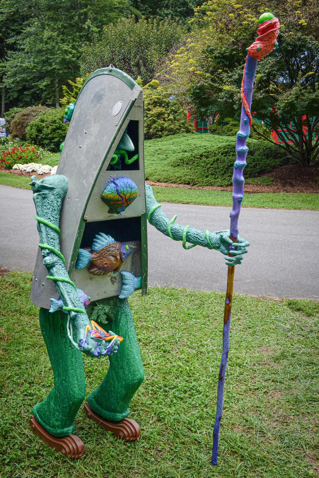 A standing green figure with a grey cabinet for a head, holding a frog and a tall purple staff.