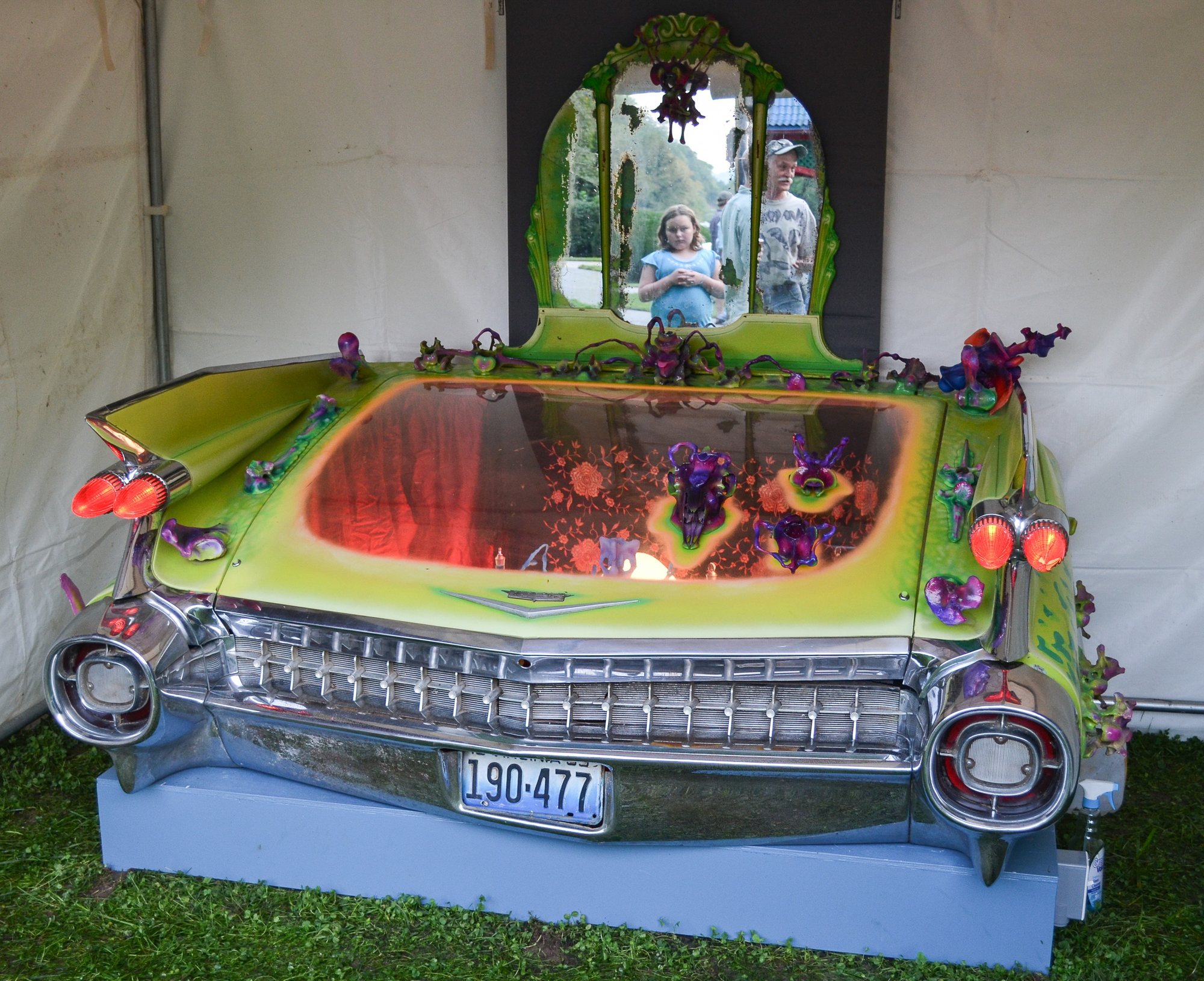 The tail fins and chrome rear of a classic car, its trunk opened into a glowing, painted scene with flowers.