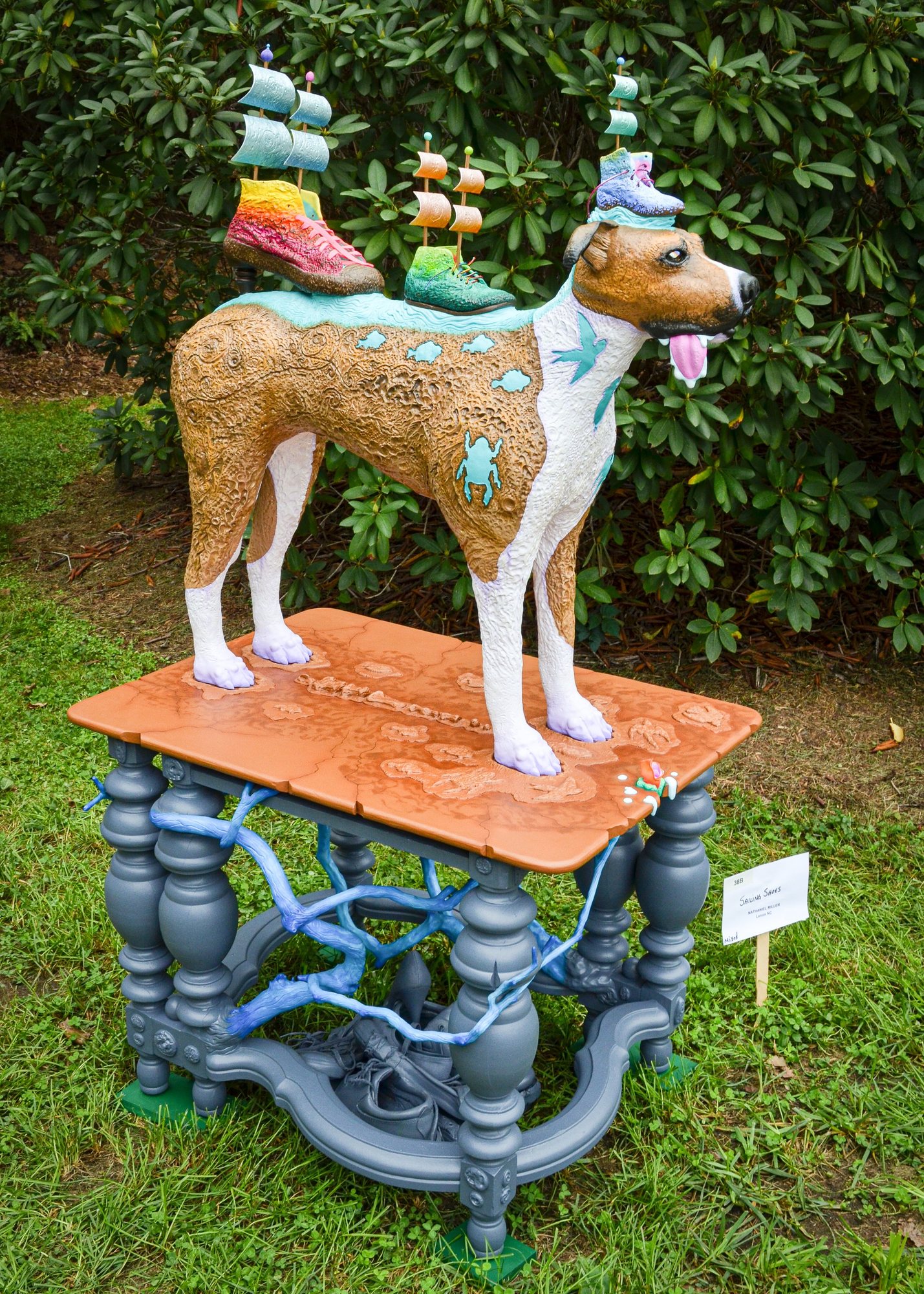 A carved dog stands on a terracotta-colored tabletop over grey turned legs, two sailing ships perched on its head.